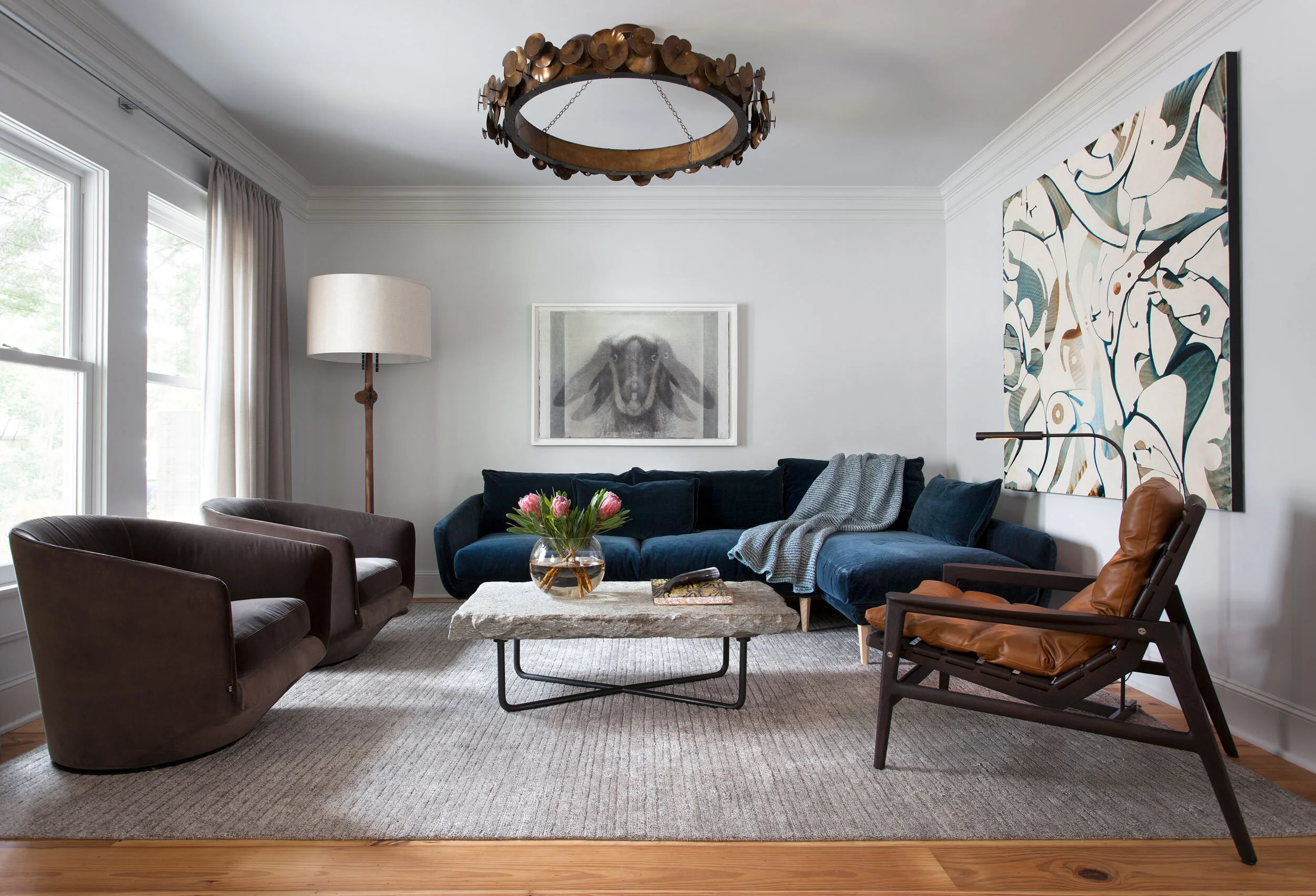 Navy curved sofa with sculptural carved wood pendant light, mid-century leather chairs, stone coffee table, and modern art