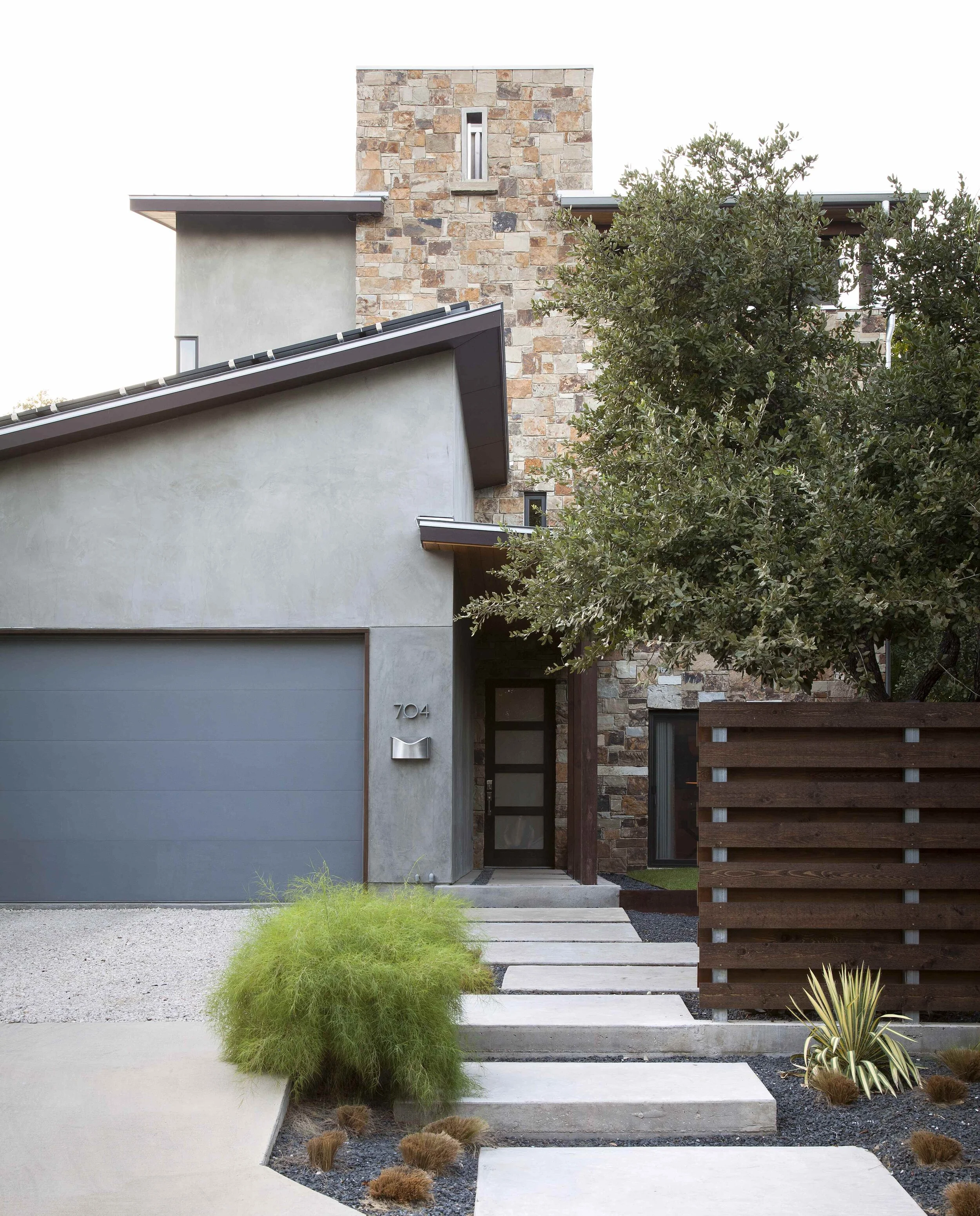 Modern home with mixed-material stone-and-concrete facade, geometric pathway, dark metal door, and contemporary landscaping