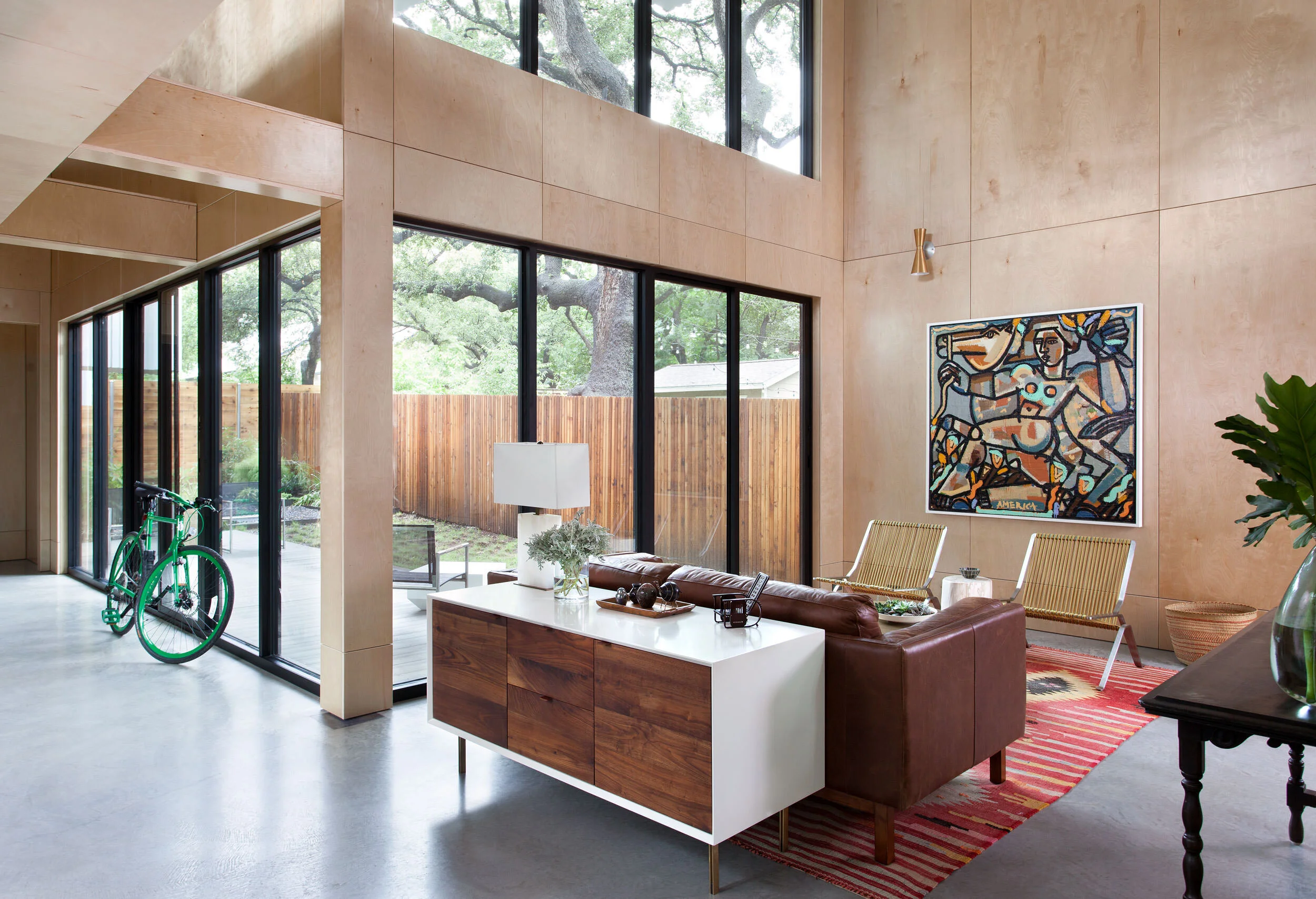 Plywood-walled room with black-frame sliding doors, polished concrete floors, and a green bicycle