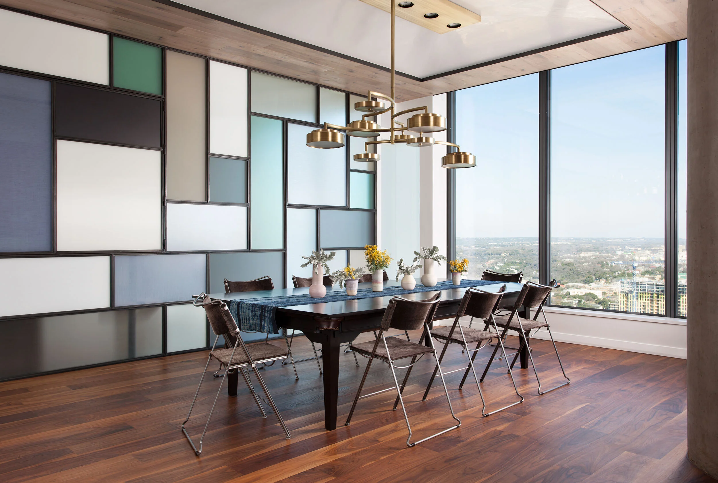Panoramic city views through floor-to-ceiling windows, black dining table, brass chandelier, geometric artwork