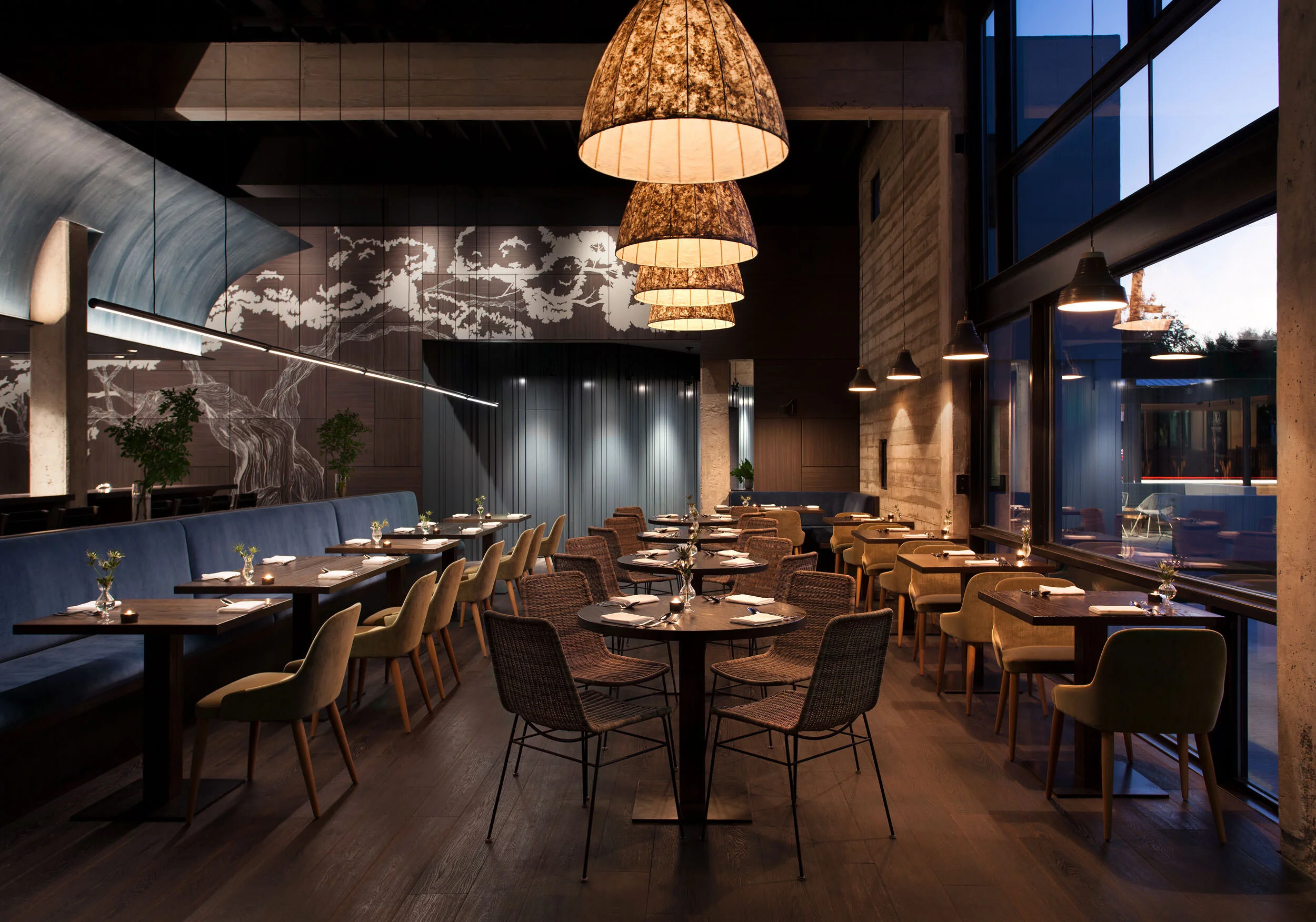 Woven brass pendant lights, blue banquette, black dining tables, dark marble walls with map detail