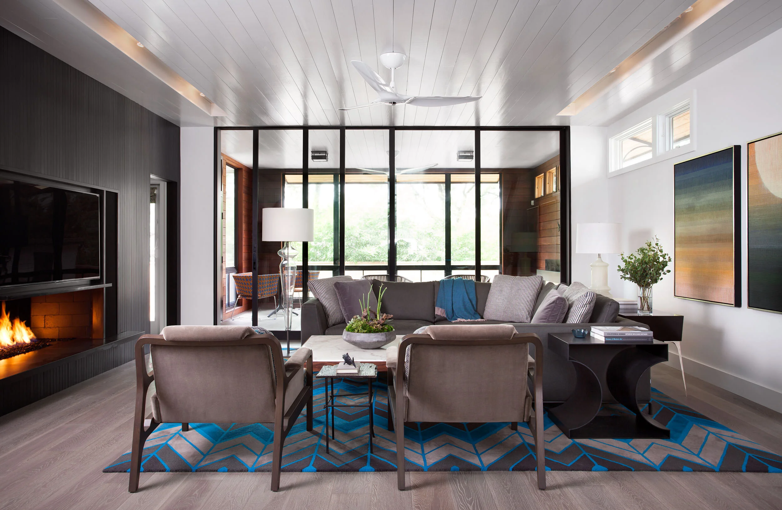 Glowing gas fireplace, gray sofa with blue accents, geometric rug, black-frame glass partition