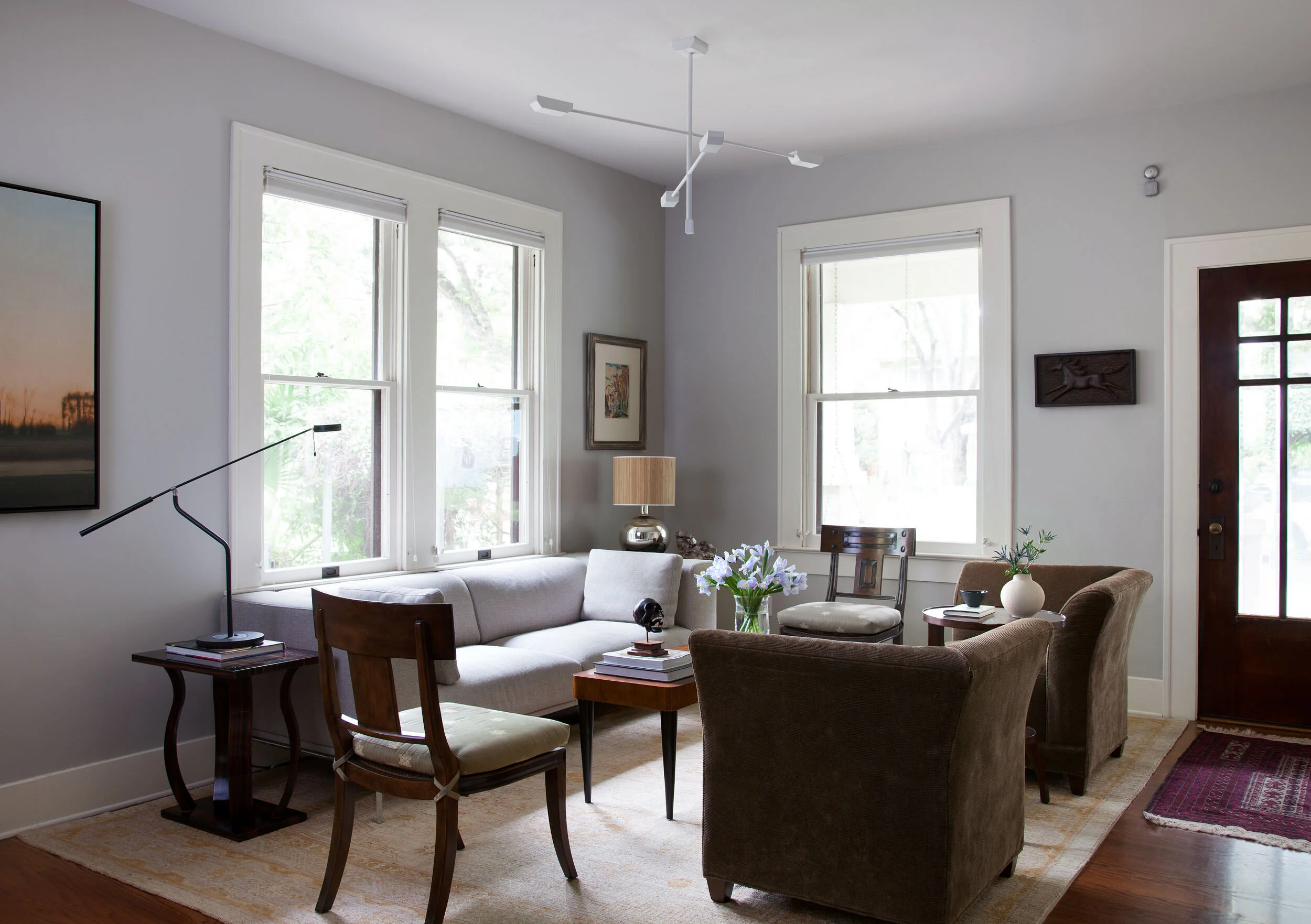 Abundant windows with green views, gray sofa, tan leather chairs, sculptural black floor lamp